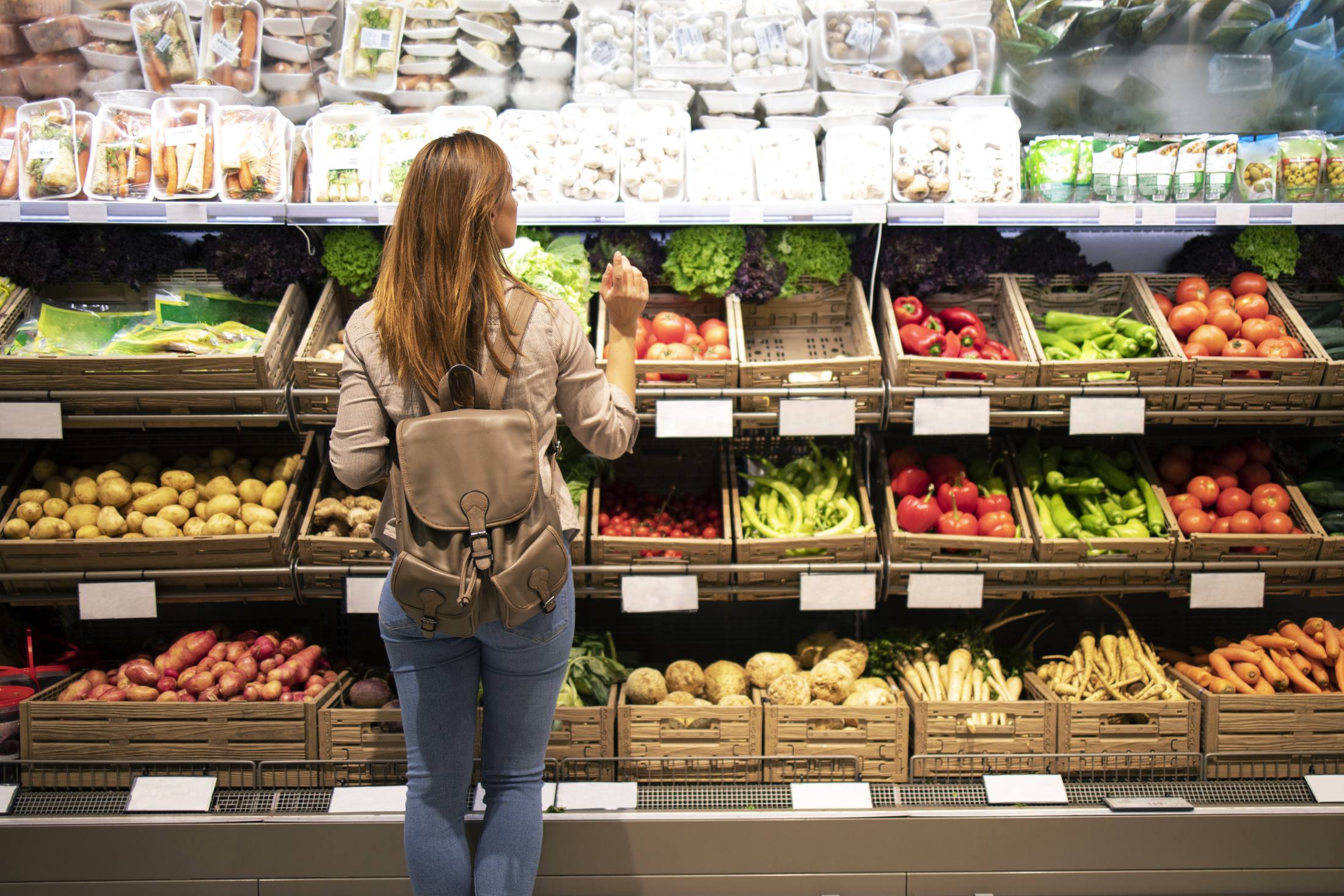 Kobieta z plecakiem wybiera składniki zbilansowanej diety czyli świeże warzywa i owoce w sklepie spożywczym
